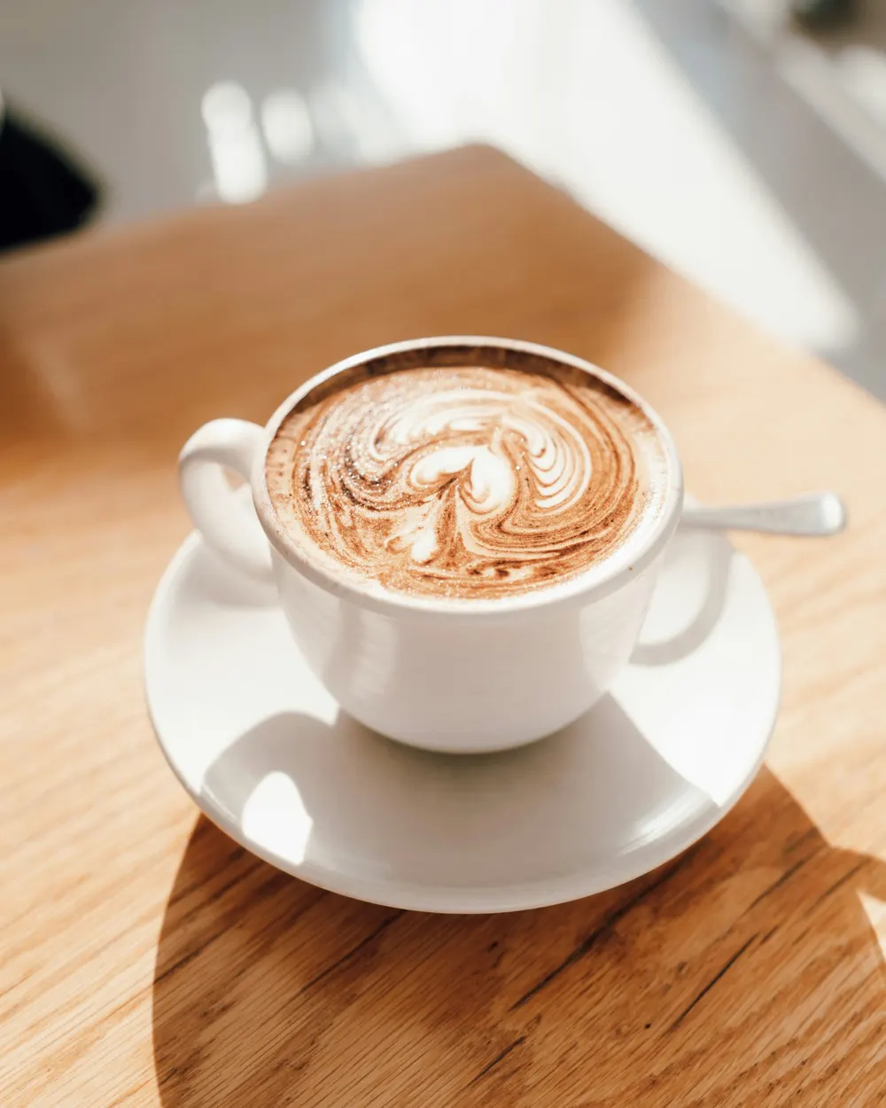 Latte with latte art in a white cup on a light wooden table